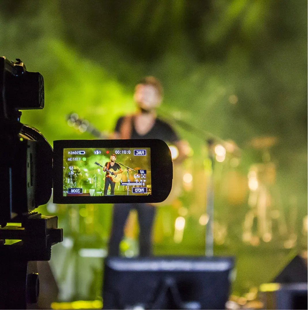 Camera screen showing a musician playing guitar and singing on stage with green lighting.