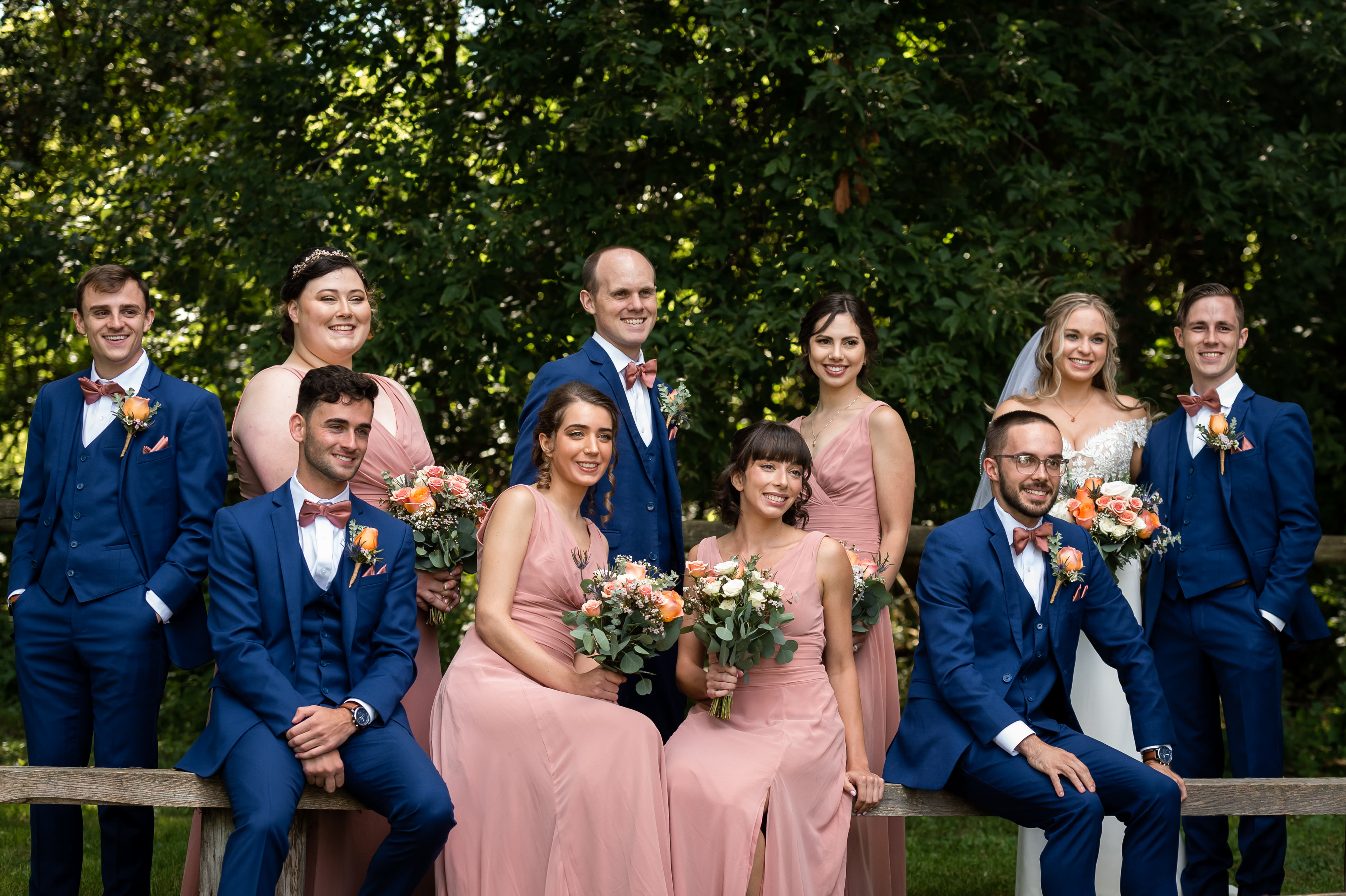 Wedding party outdoors with bride, groom, bridesmaids in pink dresses, and groomsmen in blue suits