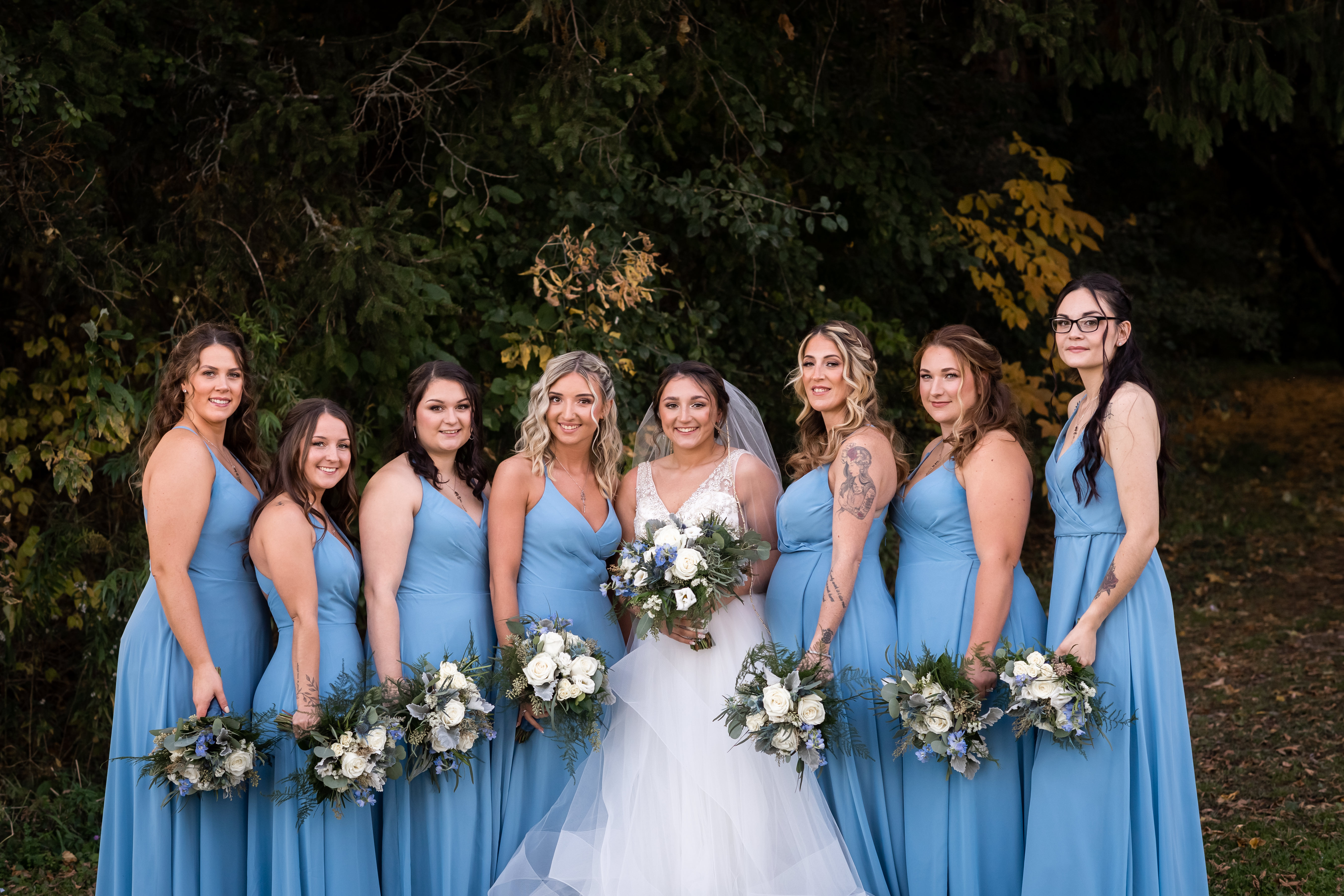 Bridesmaids in matching blue gowns posing together at a barn wedding venue