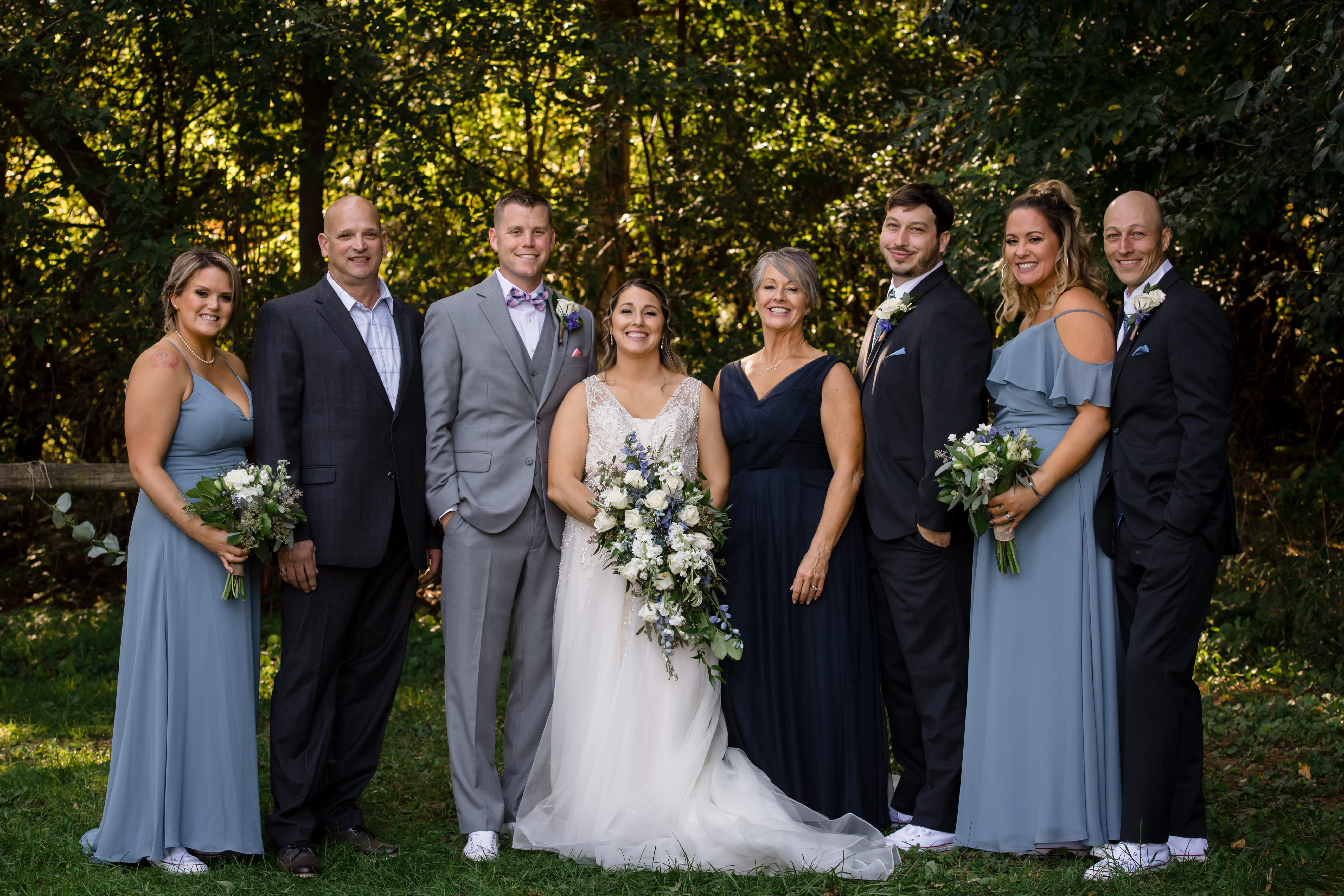 Bridal party portrait in dusty blue dresses under trees at a rustic New York wedding venue