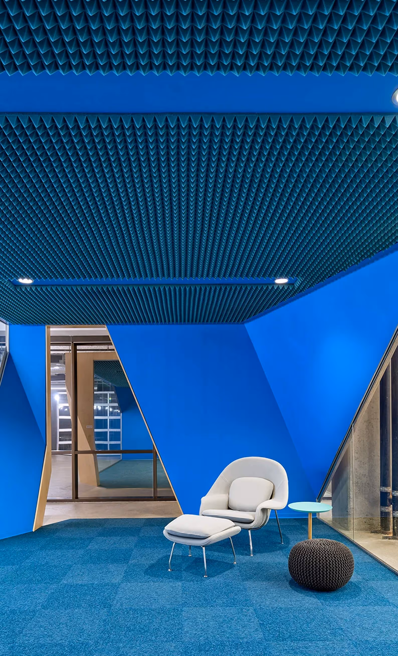Modern blue room with textured ceiling, a white lounge chair and ottoman, small table, and knitted pouf.