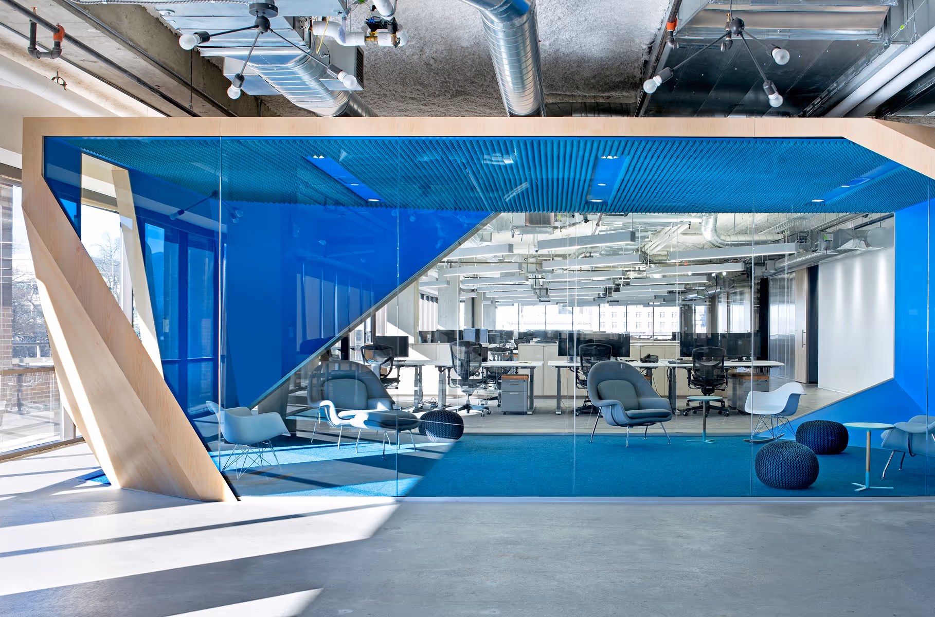 Modern office space with glass walls, blue carpet, chairs, and computer desks in background.