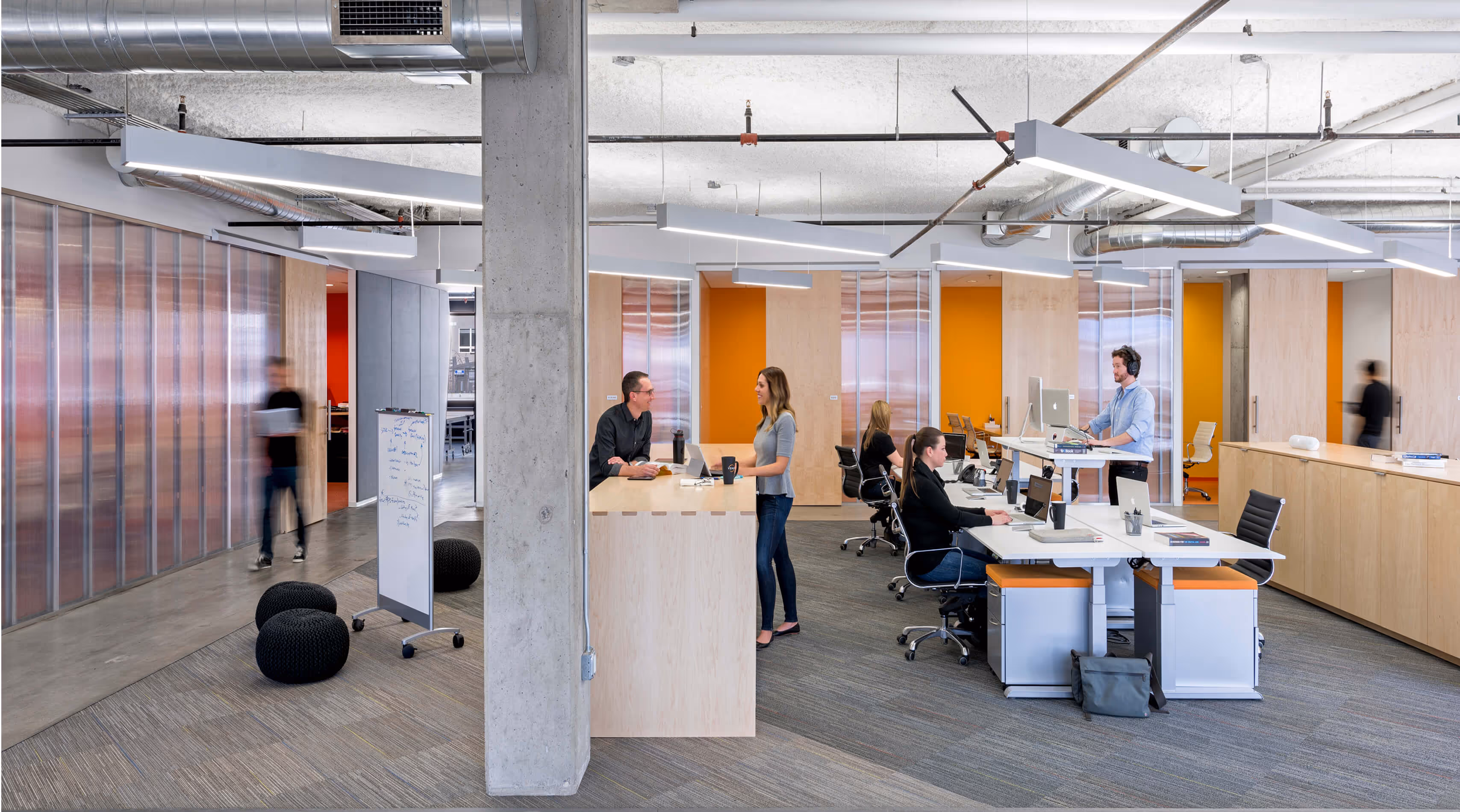 Modern open office with people working at desks and standing while having discussions.