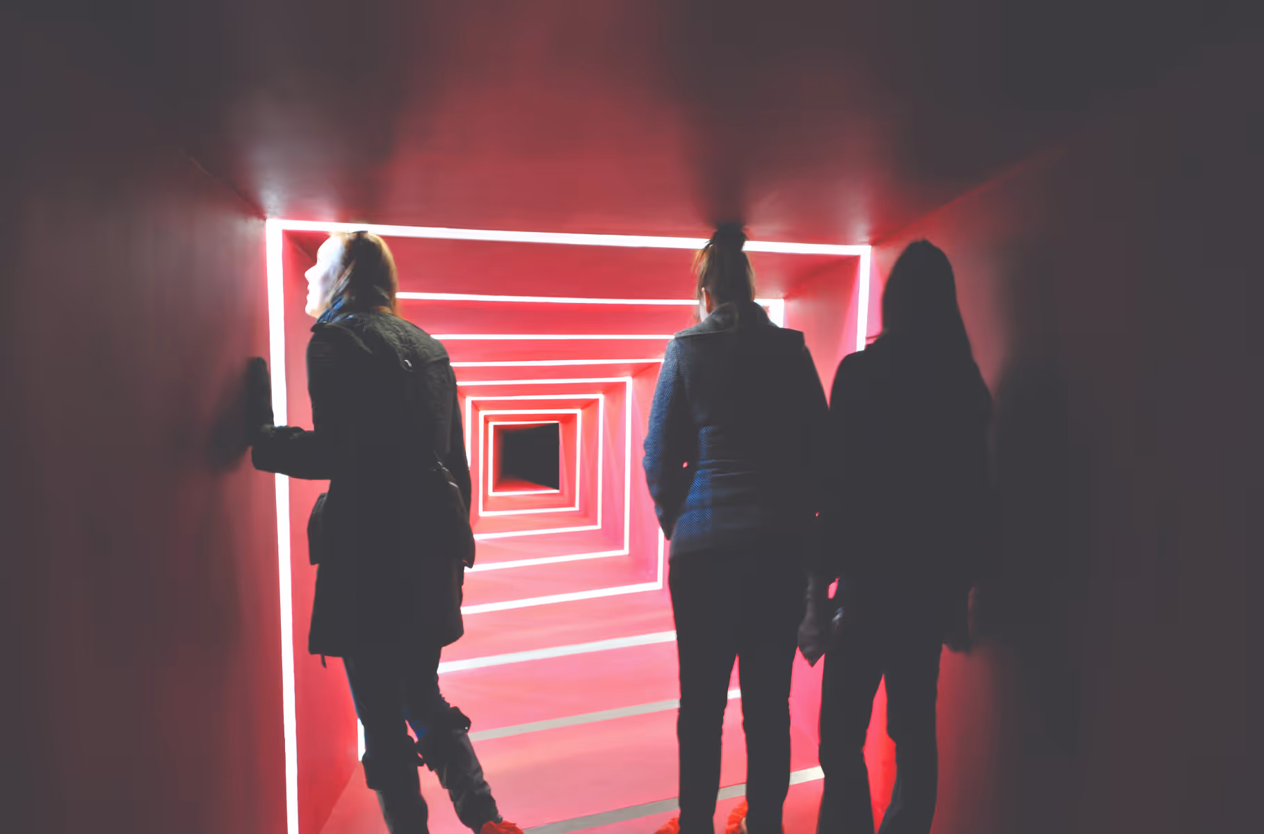 Three people walking through a glowing red and white geometric tunnel installation.