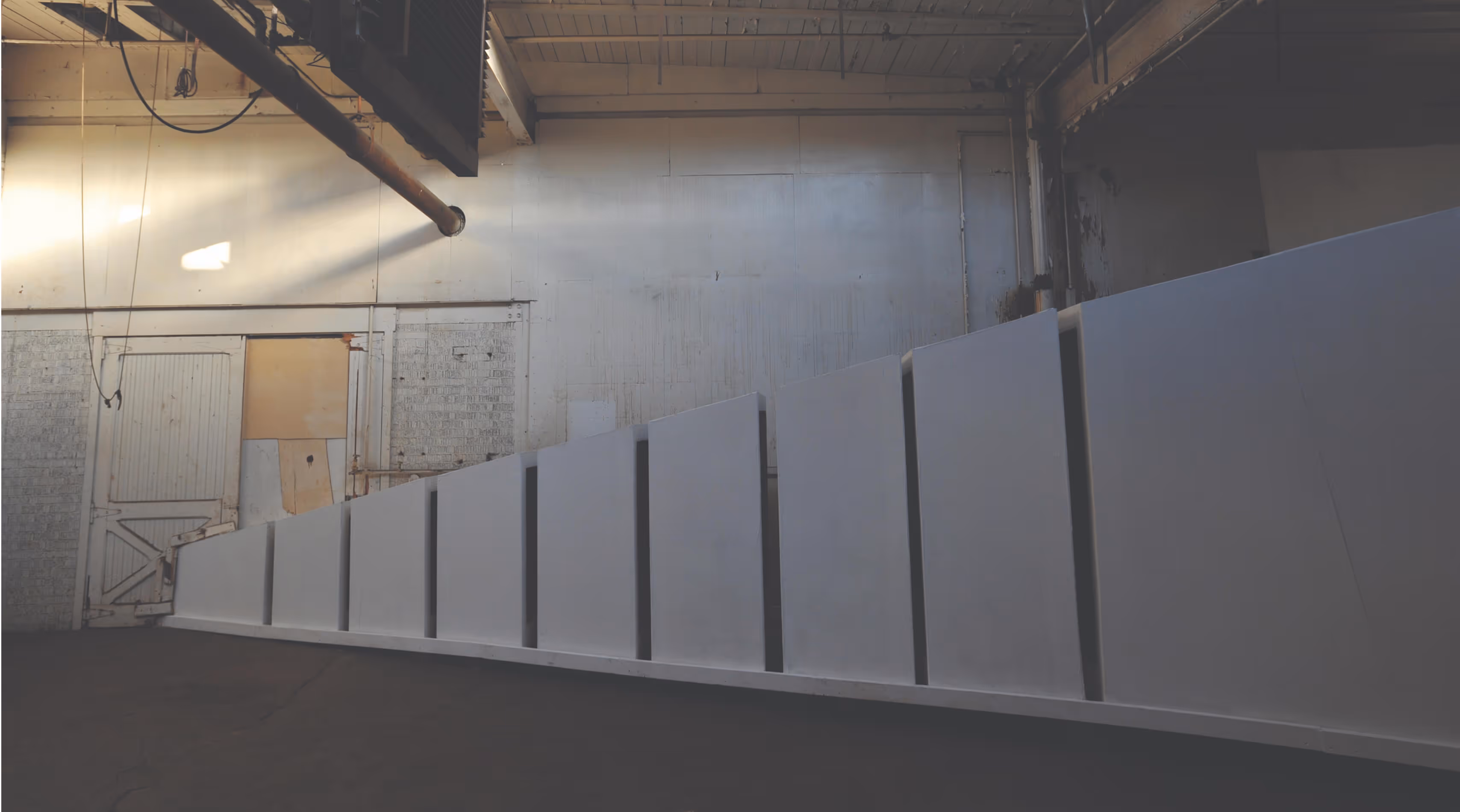 Modern art installation of angular white panels arranged in a stepped pattern inside an industrial space.