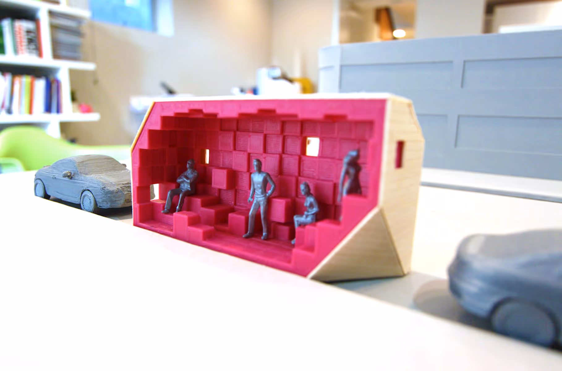 Miniature model of a room with red walls and small gray human figures seated inside.