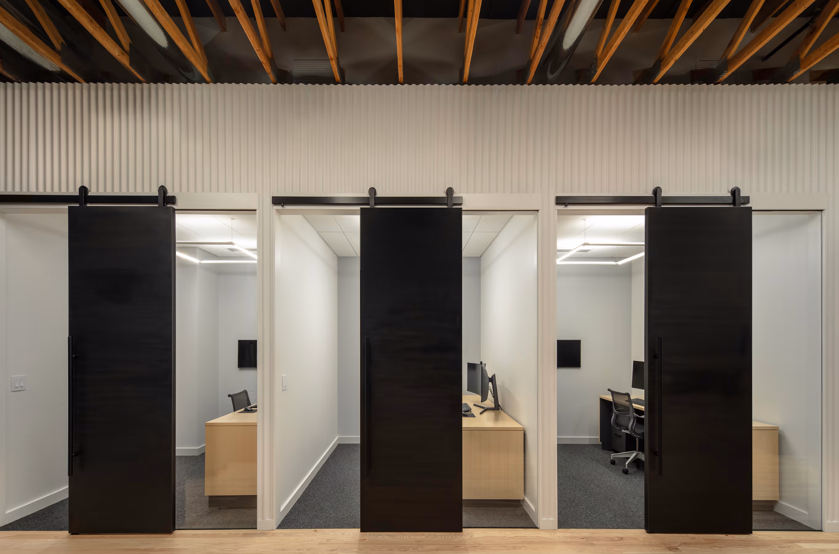 Three small modern office rooms with black sliding doors and desks with monitors inside.