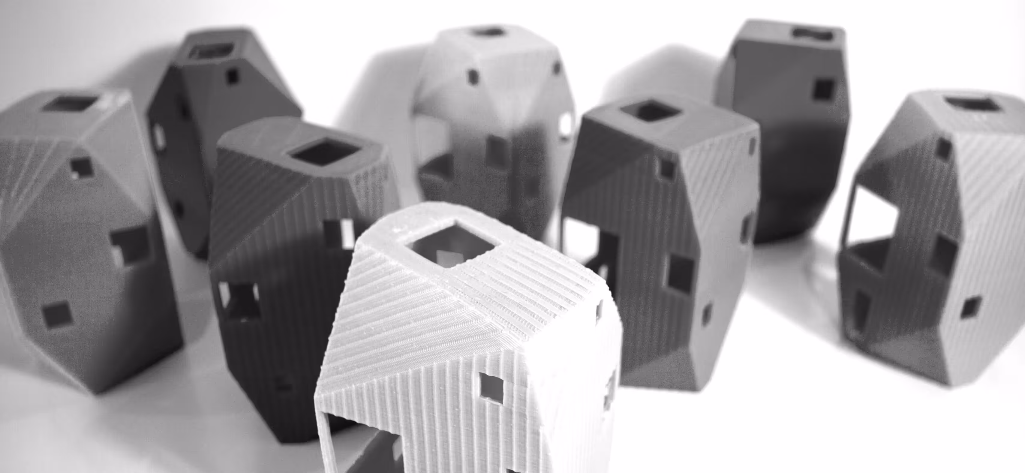 Small 3D-printed house models with geometric shapes and square windows arranged together.