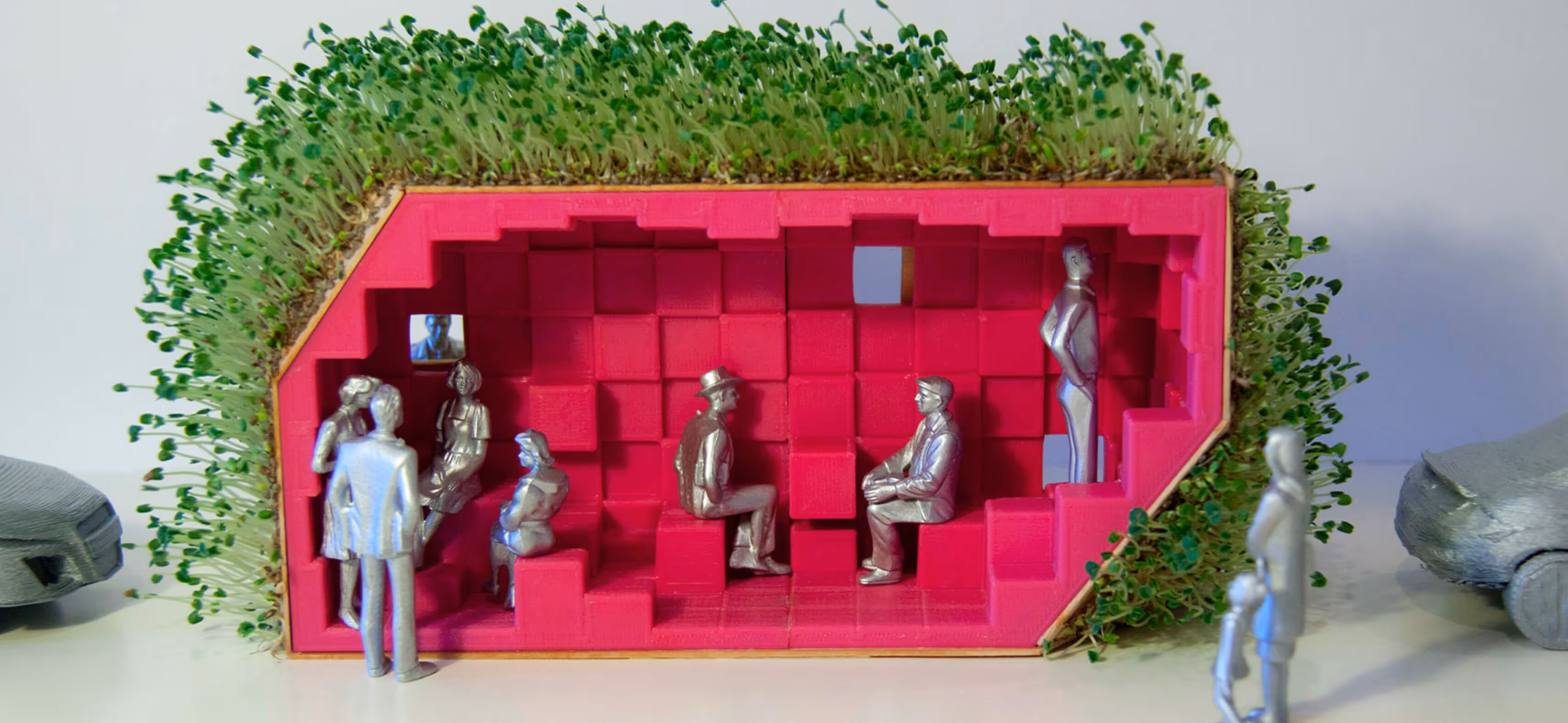Model of a red interior with silver human figures inside and green plants growing around the exterior.