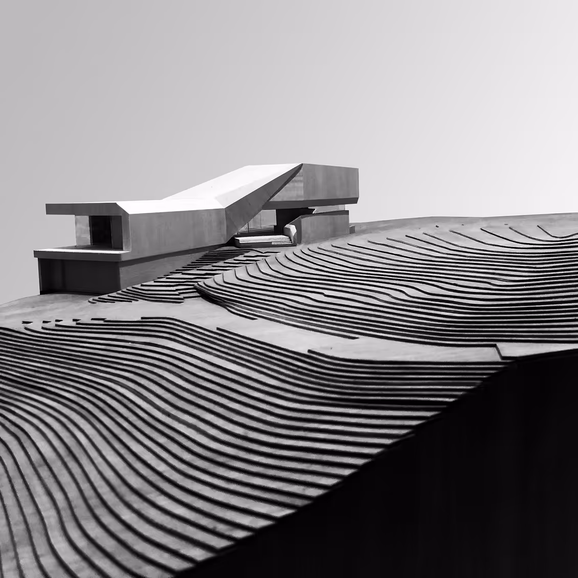 Modern architectural model of a building on a topographic terrain with curved contour lines.