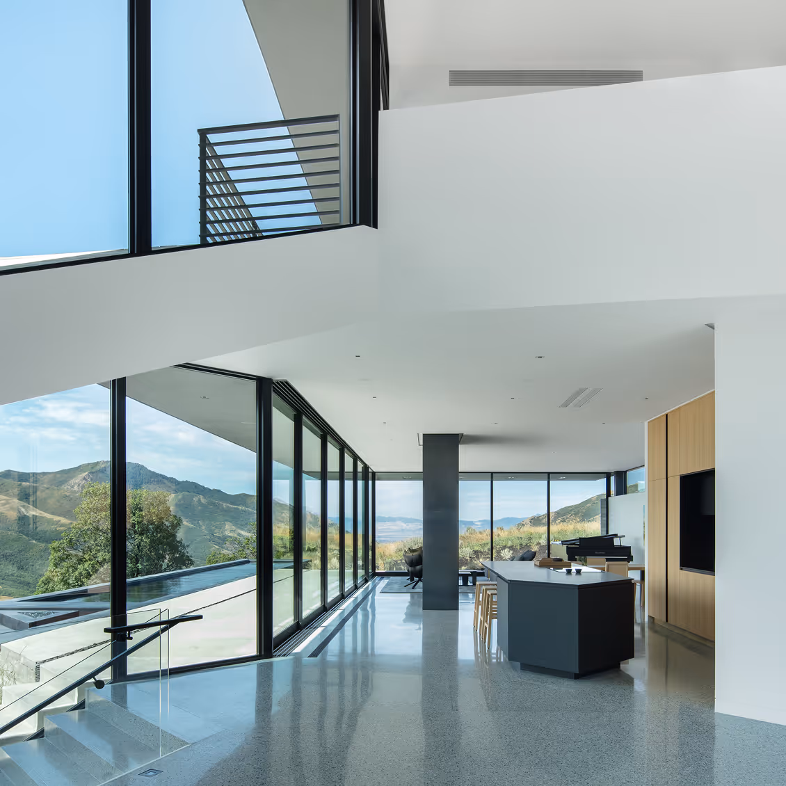 Modern open living space with large glass windows showing mountain views and a kitchen island with stools.