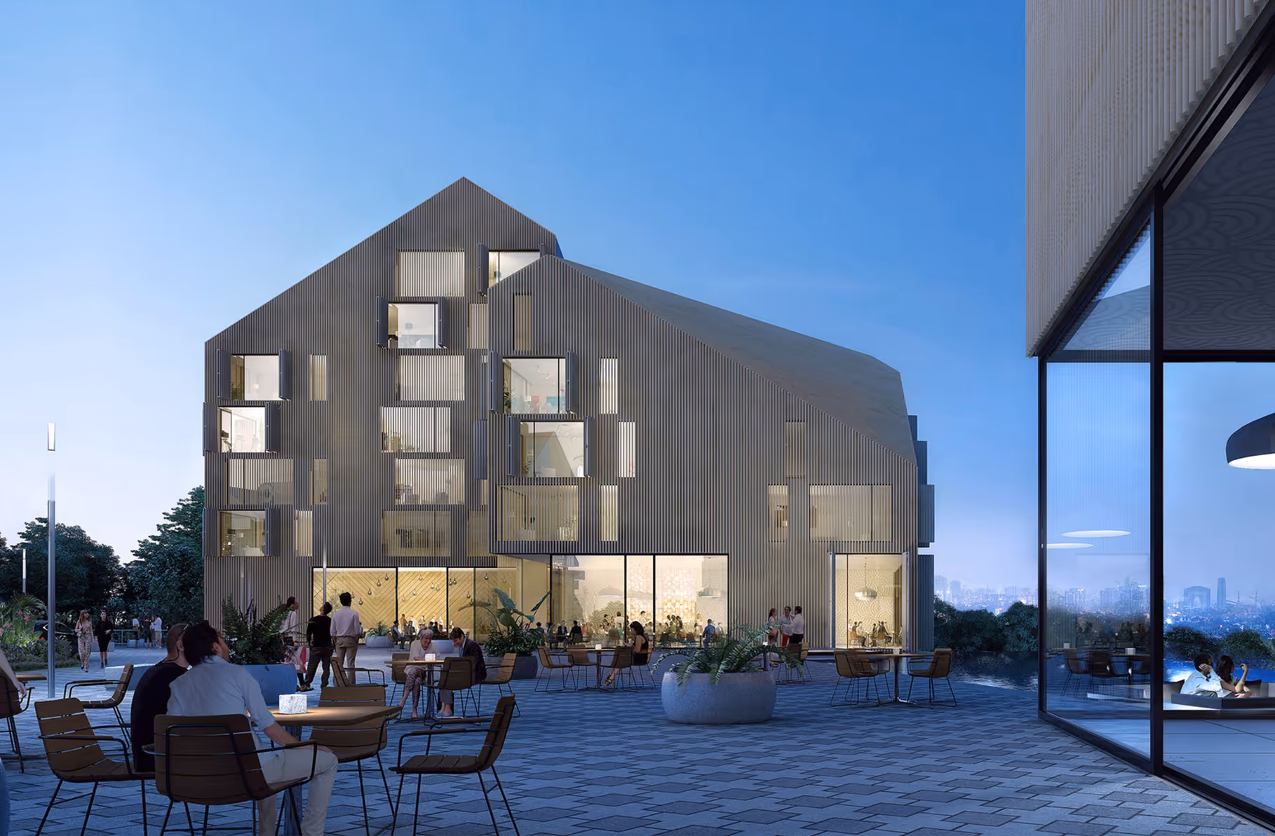 Modern building with illuminated windows and outdoor seating area under a clear evening sky.