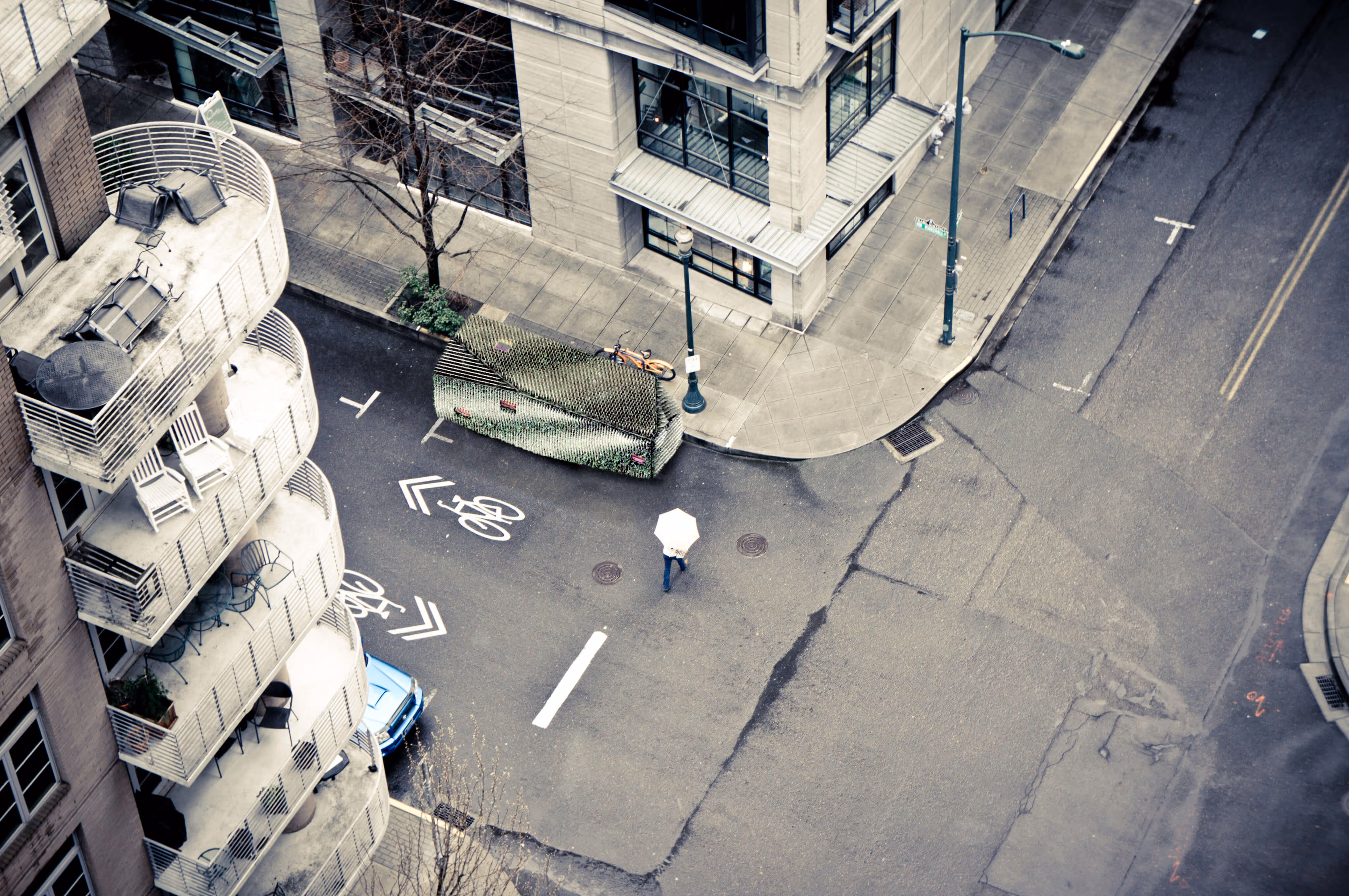 Person with white umbrella crossing an empty urban street with bike lane markings and curved balconies.