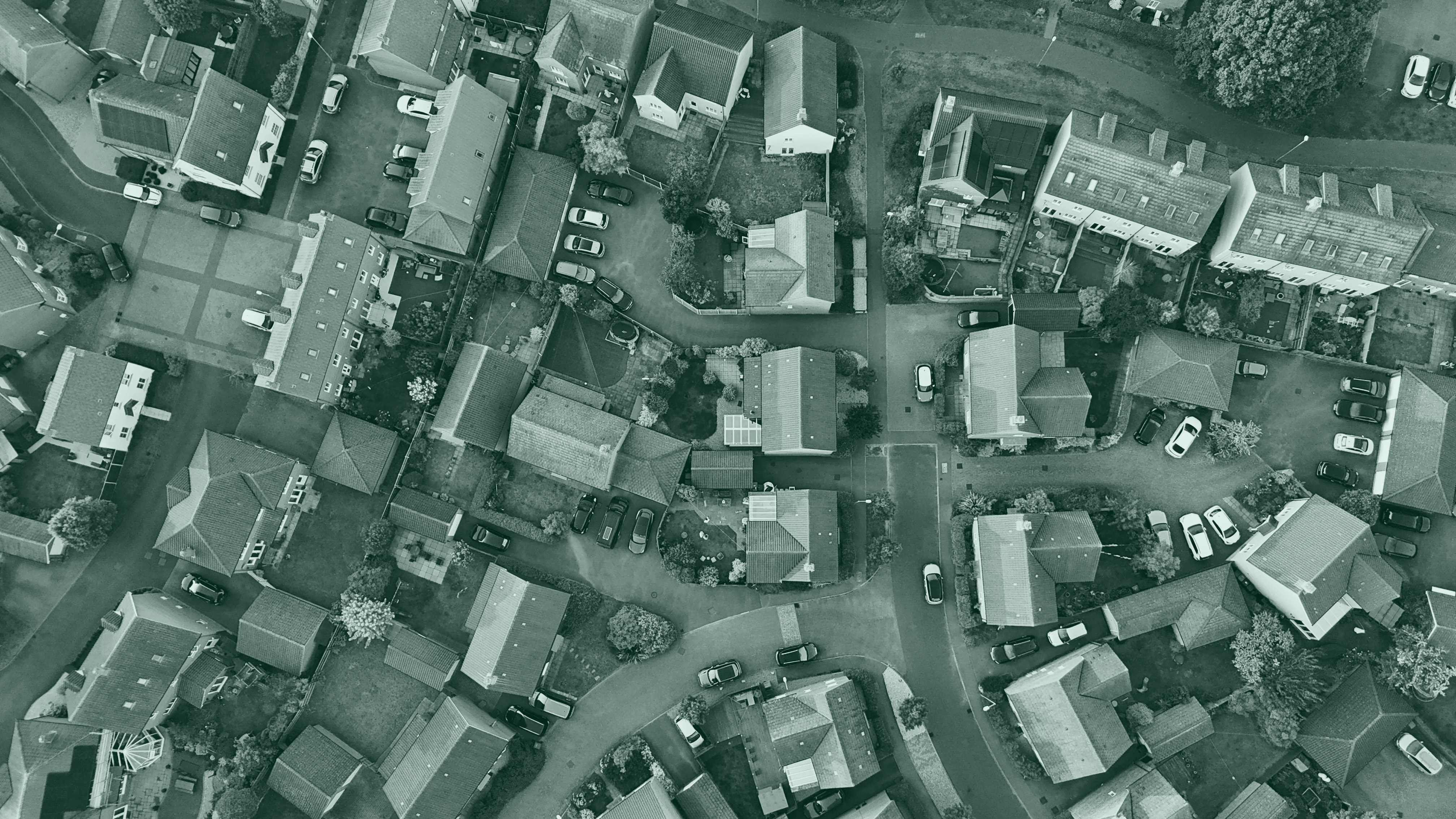 A top-down aerial view of a suburban residential neighborhood showing houses, streets, and parked cars.