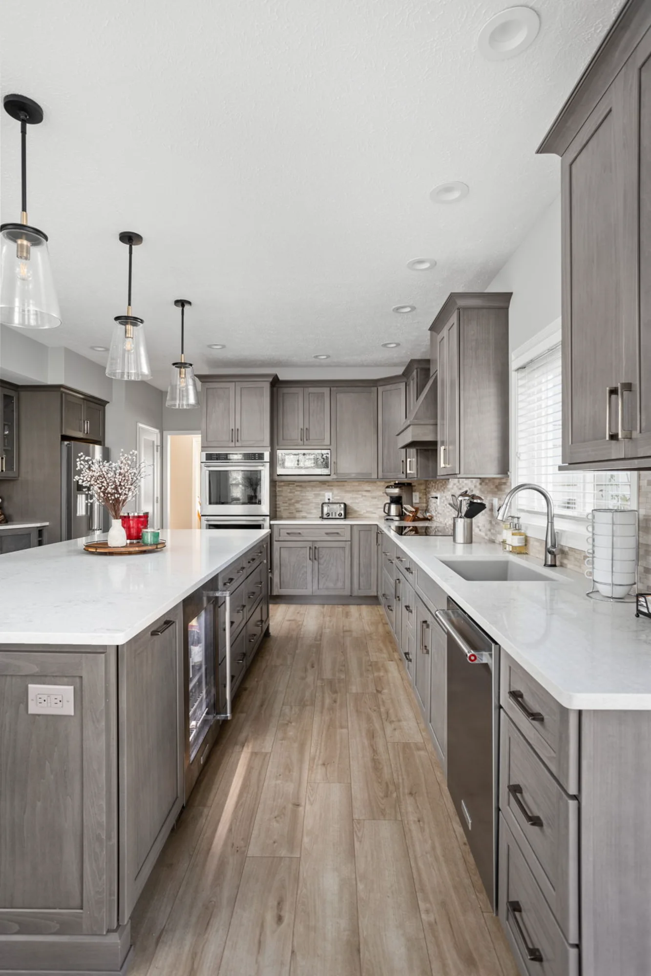 Narrow kitchen with gray cabinets, pendant lights, and long countertop