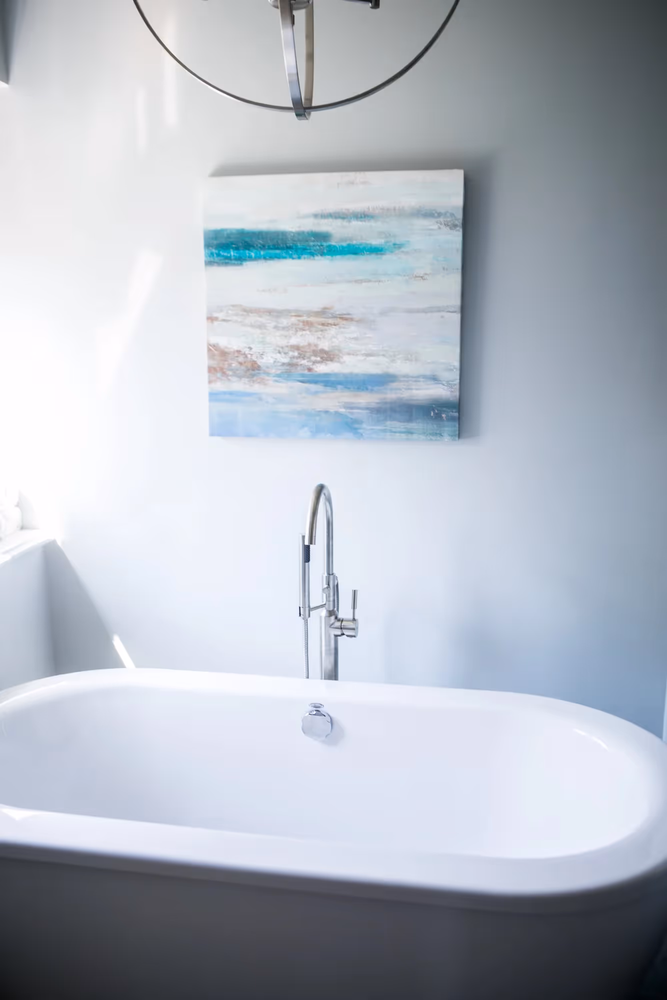 Minimalist bathroom with freestanding tub and framed coastal artwork.