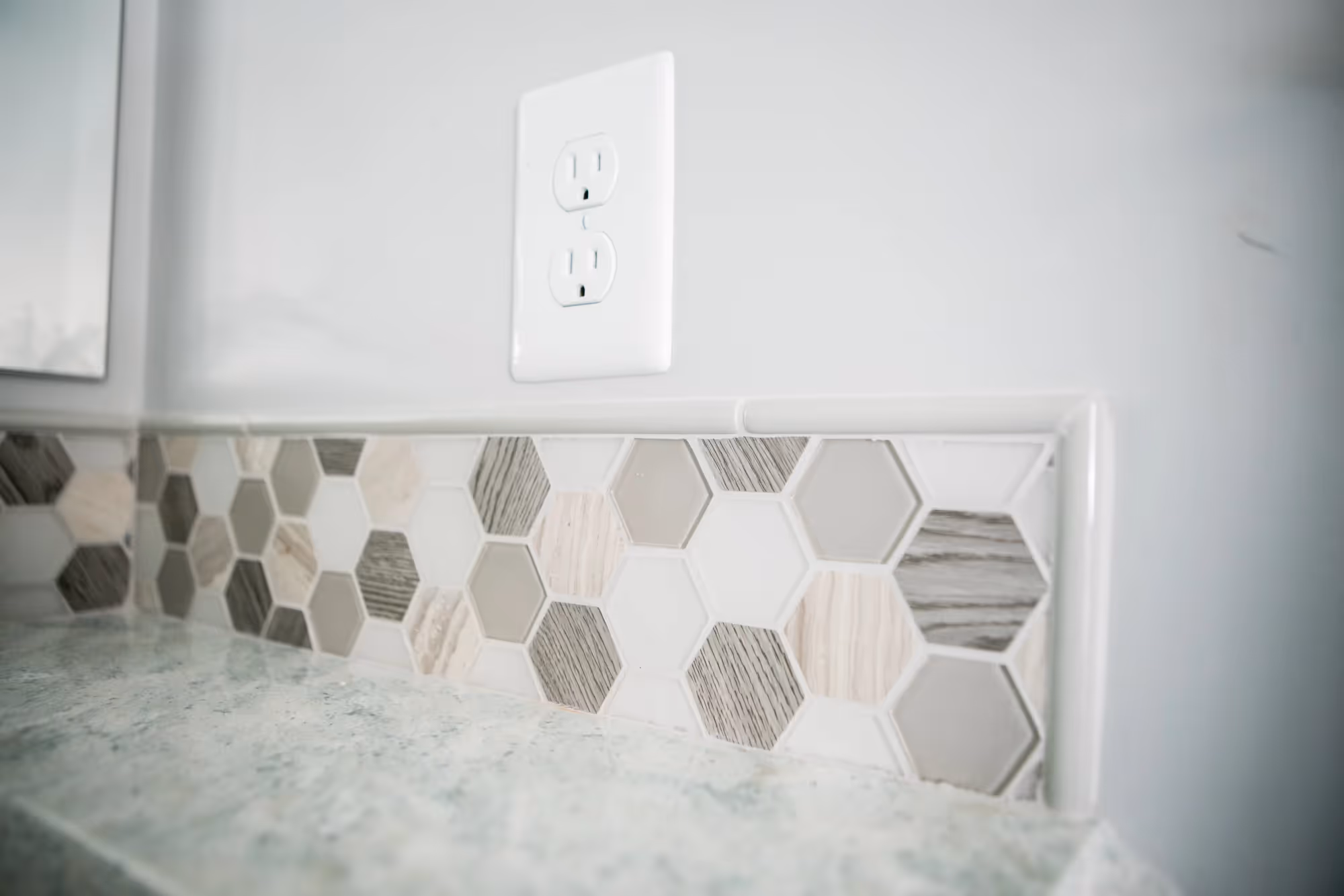 Close-up of a wall outlet and hexagon tile backsplash.