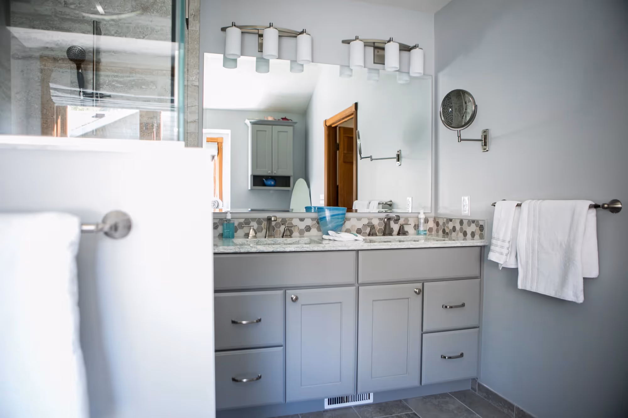 Modern bathroom with double sinks, mirrors, and gray cabinets.