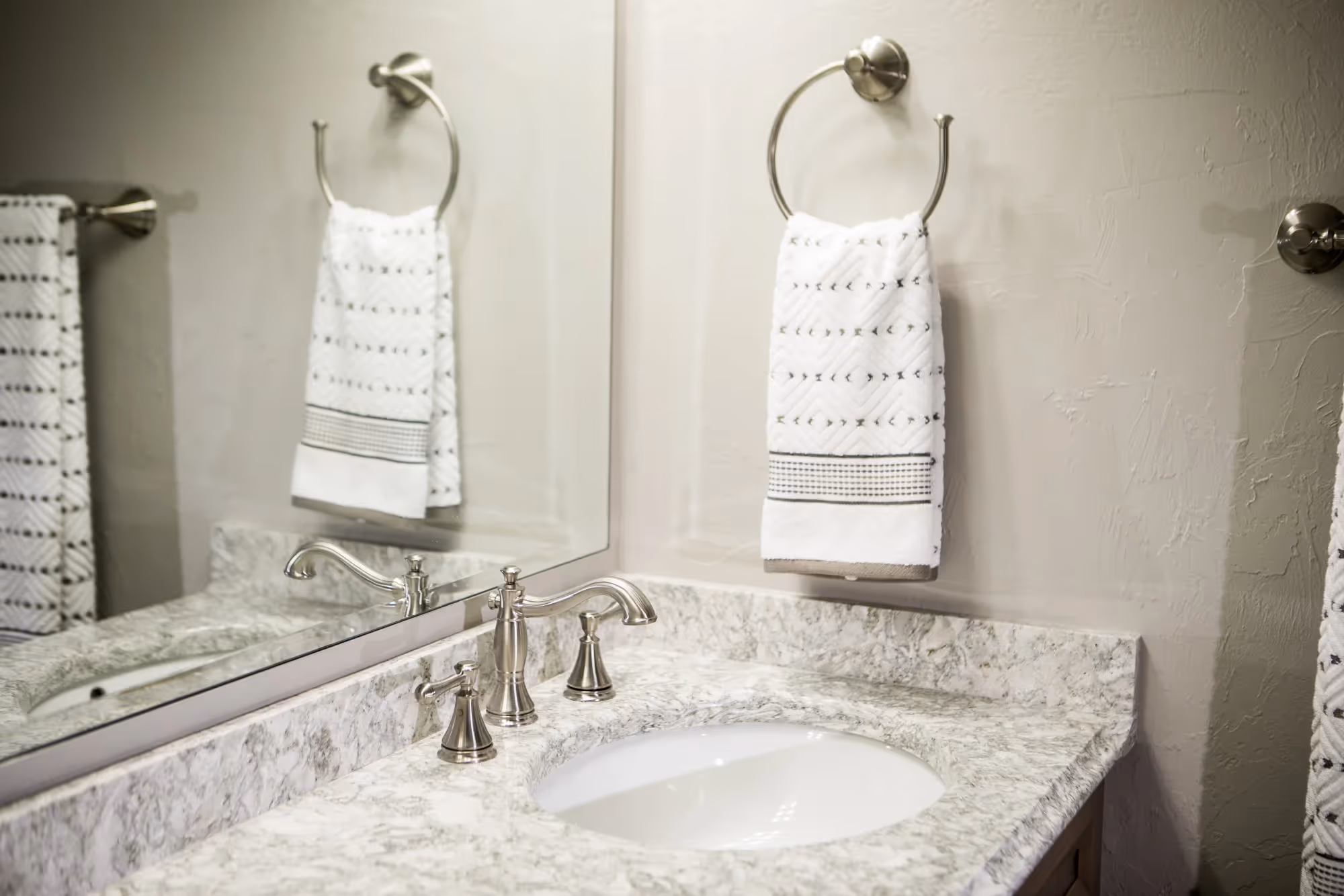 Bathroom vanity with granite countertop, sink, and two hanging towels.