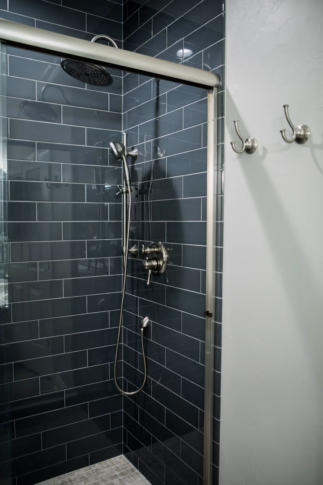 Modern bathroom with dark tiled shower and glass door.