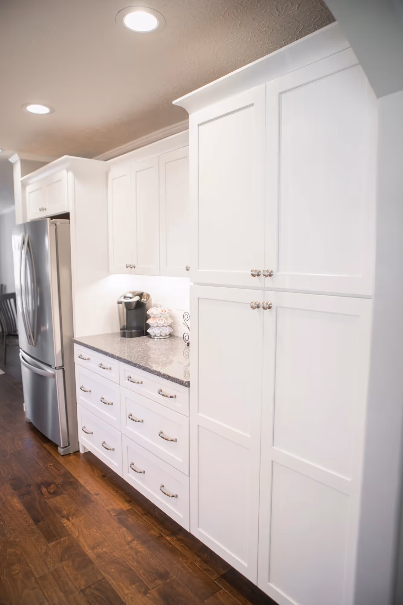 Narrow kitchen hallway with white cabinetry and wooden flooring.