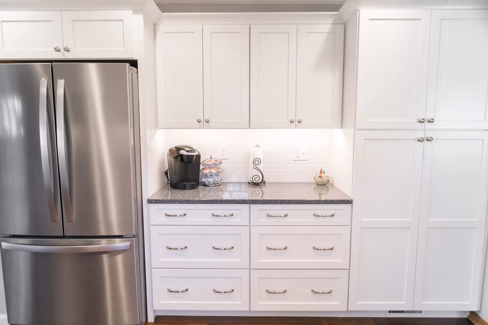 Stainless steel refrigerator next to white pantry cabinets