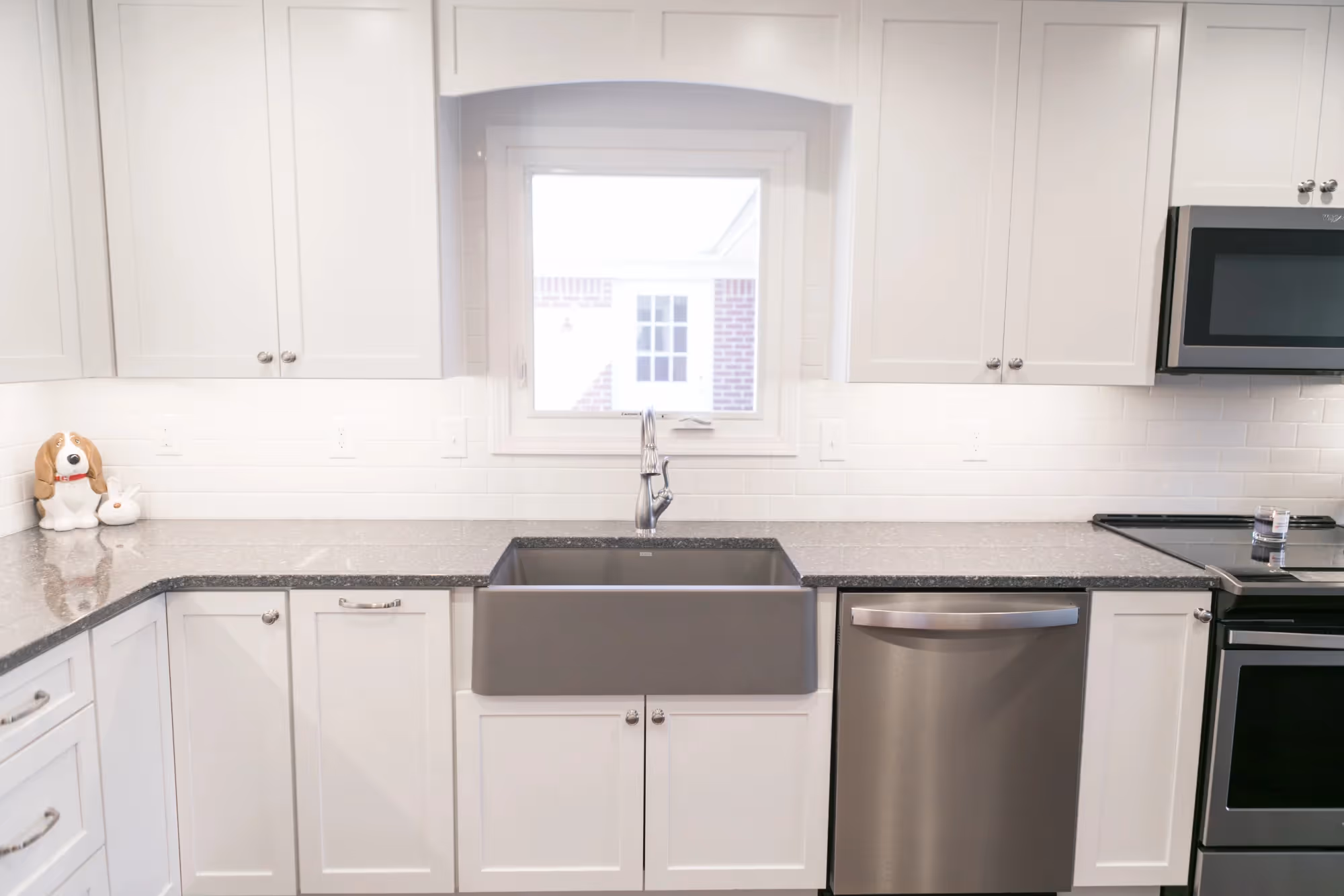 White kitchen interior with marble countertop and farmhouse sink.