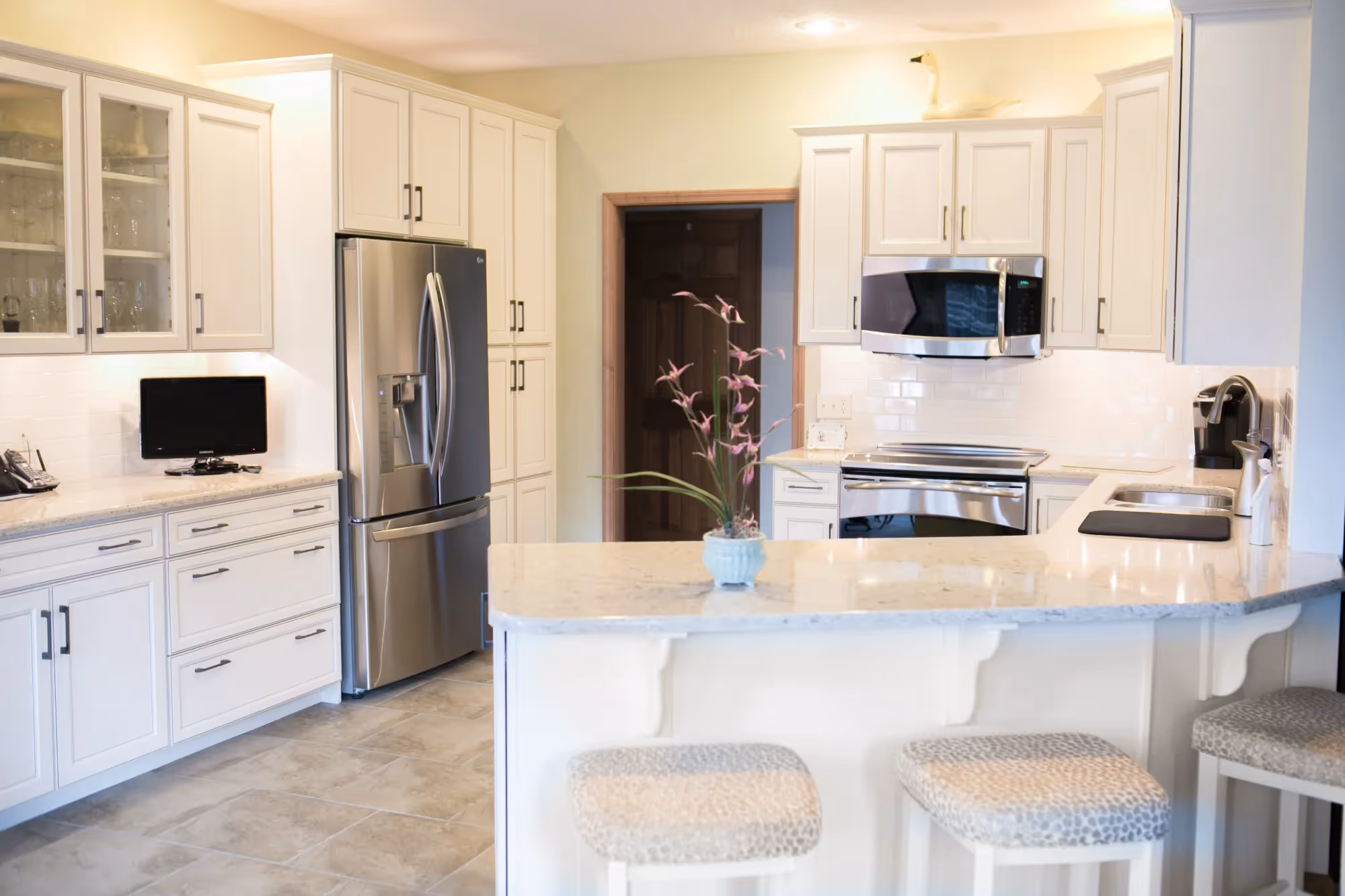 Bright white kitchen with island and stainless steel refrigerator