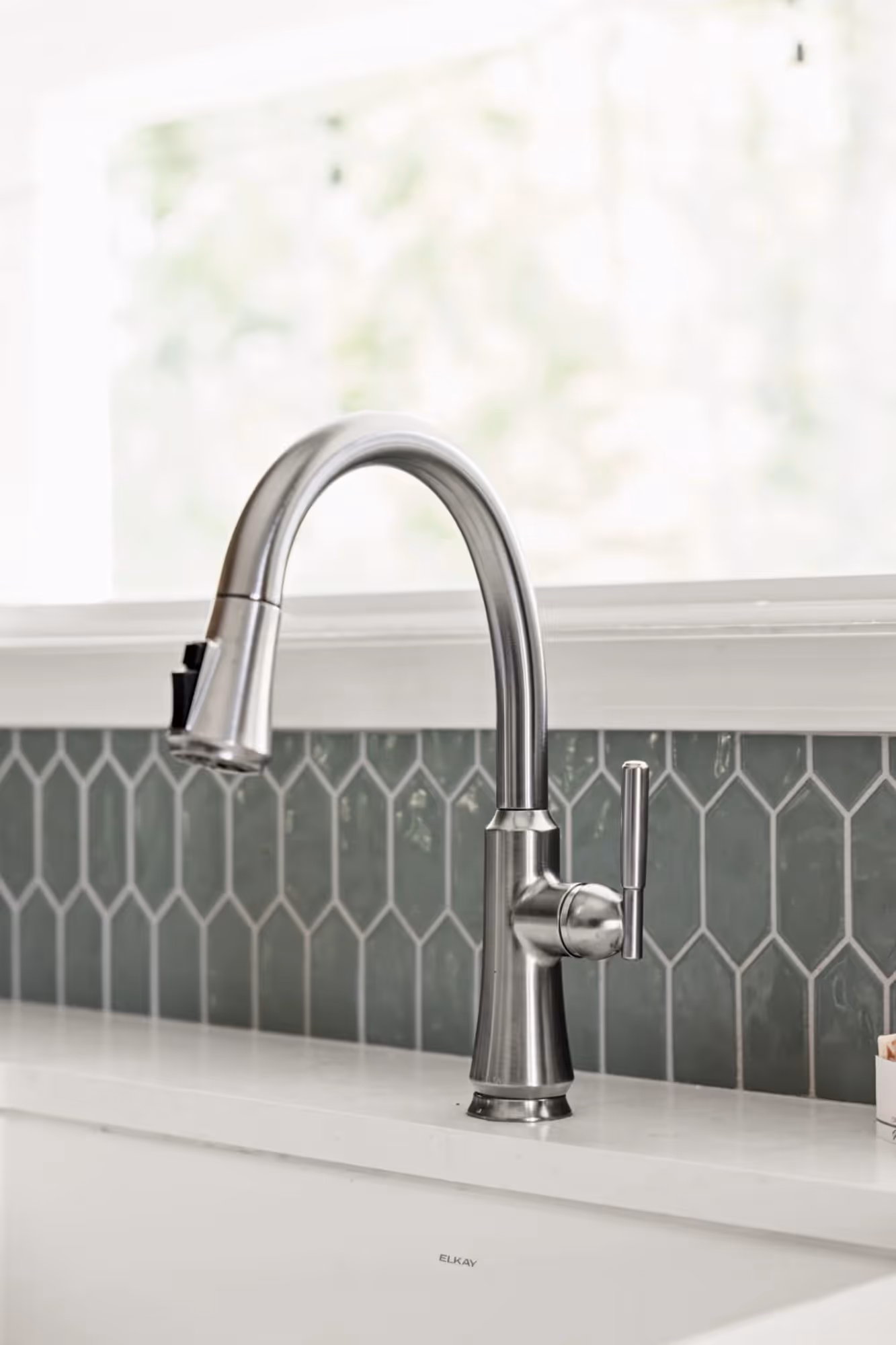 Kitchen sink with metallic faucet and tiled backsplash.