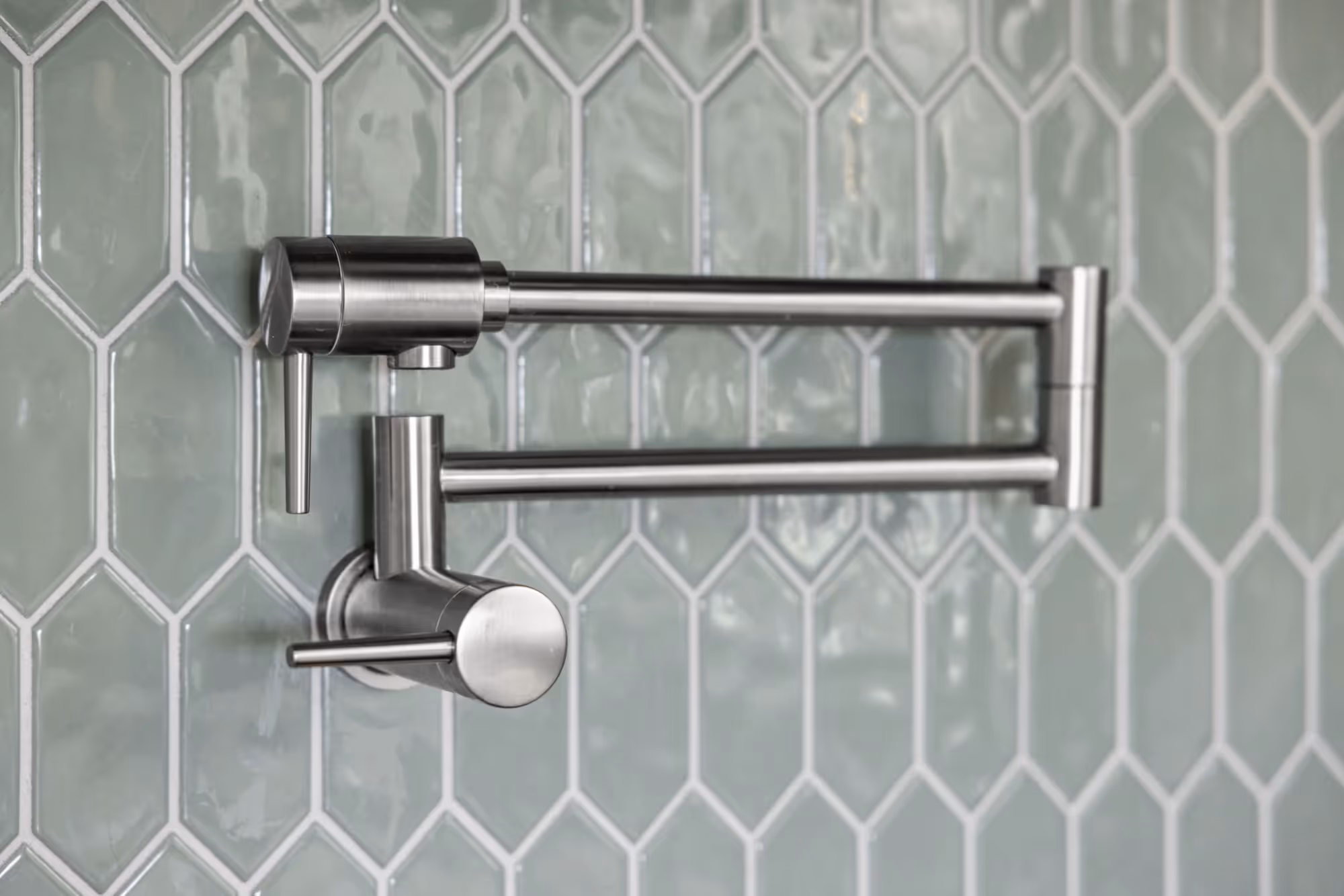 Wall-mounted faucet over teal hexagon tile backsplash