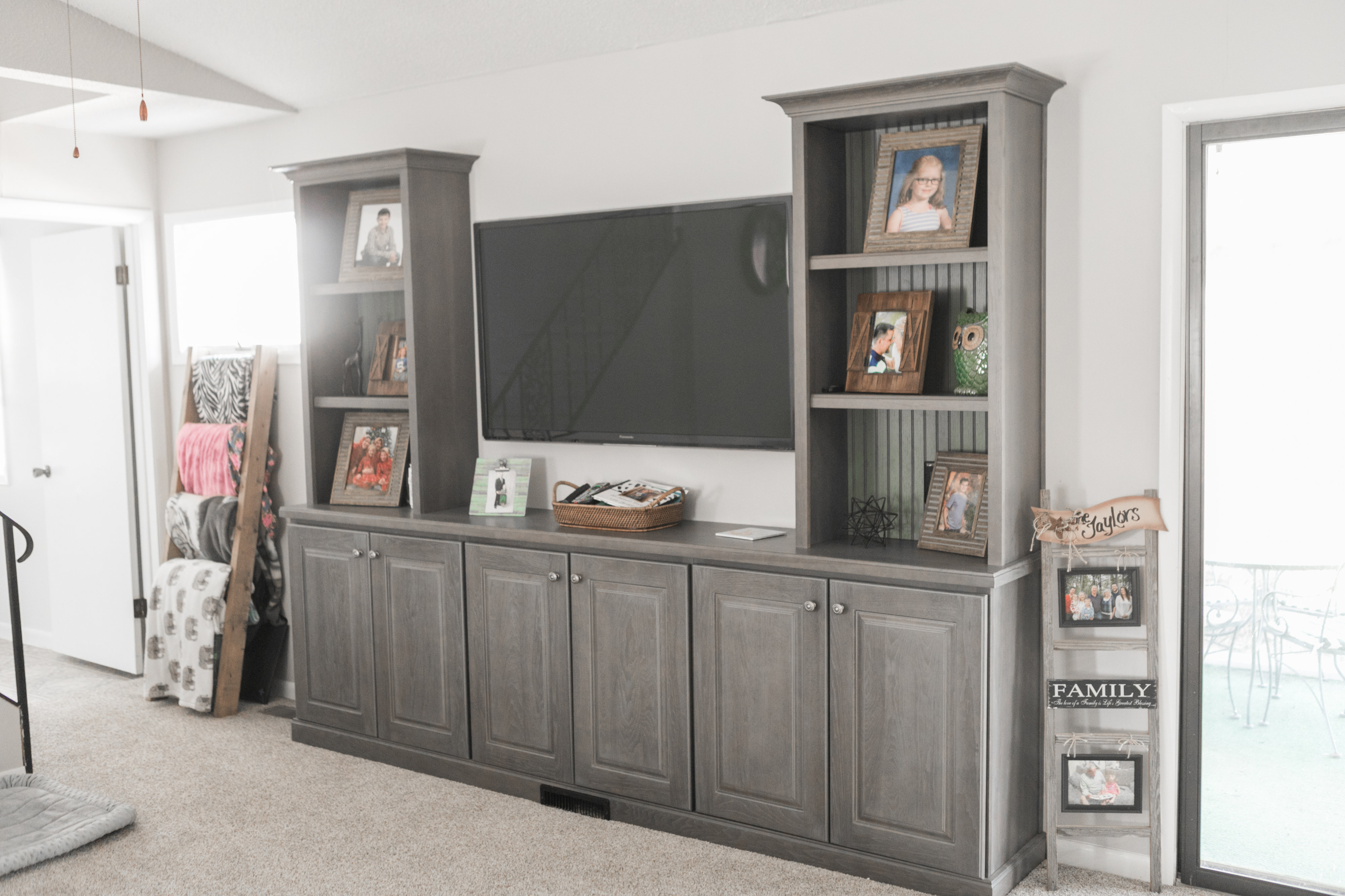 Living room with large TV, shelving, and gray cabinetry.