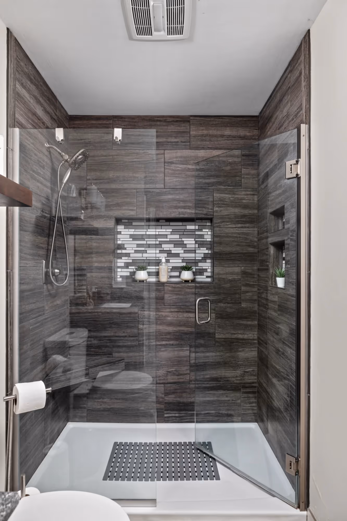 Narrow walk-in shower with dark tile and glass door