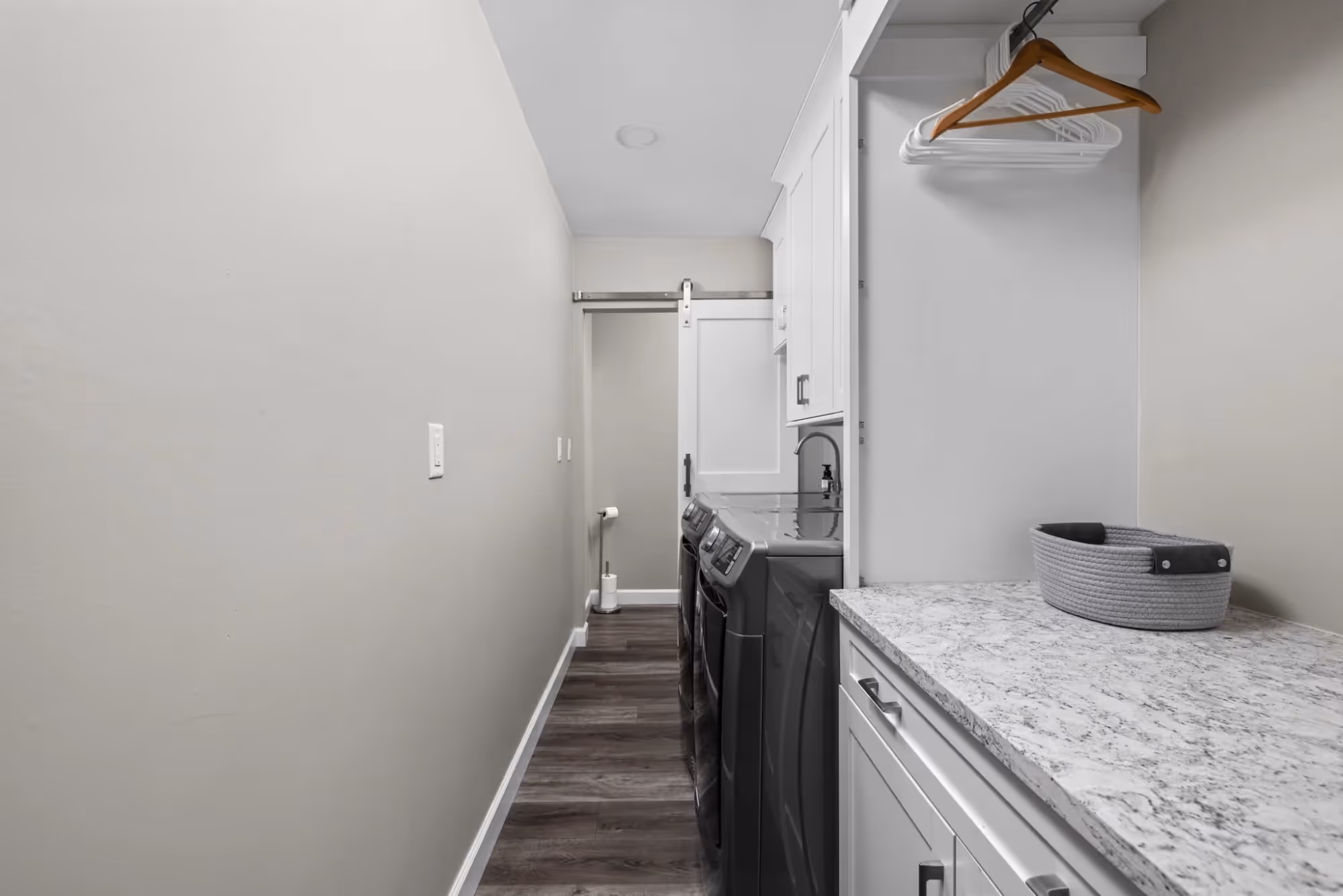 Narrow hallway with white walls, vanity, and wood flooring.