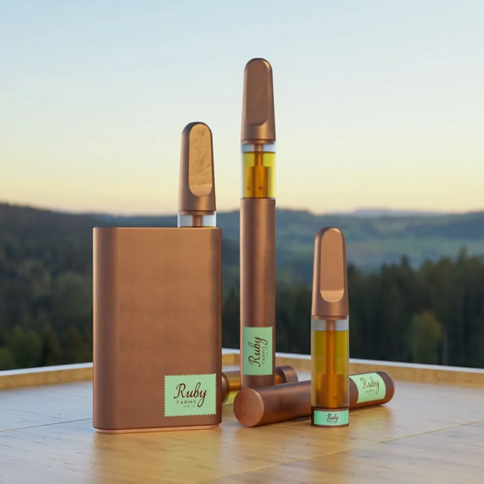 Bronze vape pens and cartridge with amber oil, labeled Ruby Farms, on wooden surface with forest background.