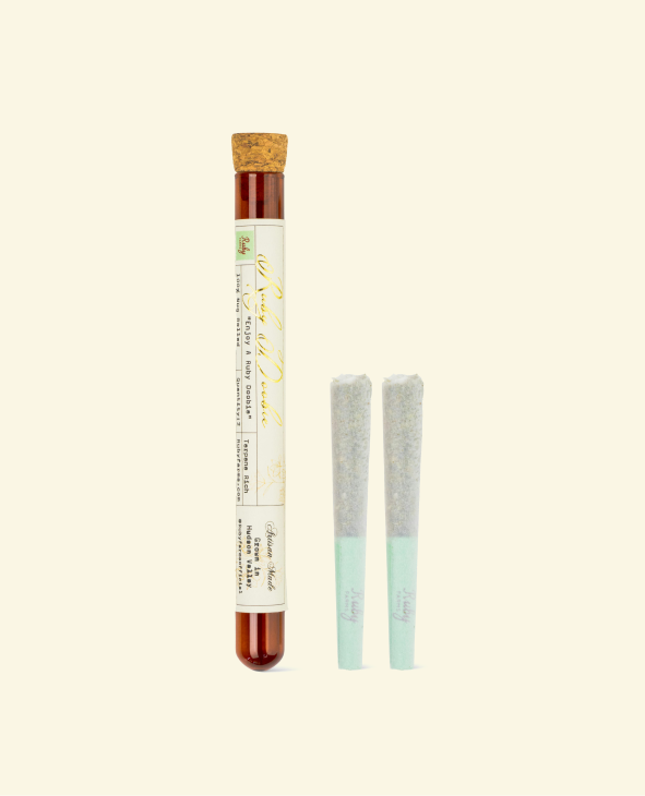 Two pre-rolled joints next to a sealed cylindrical glass container with a cork stopper.