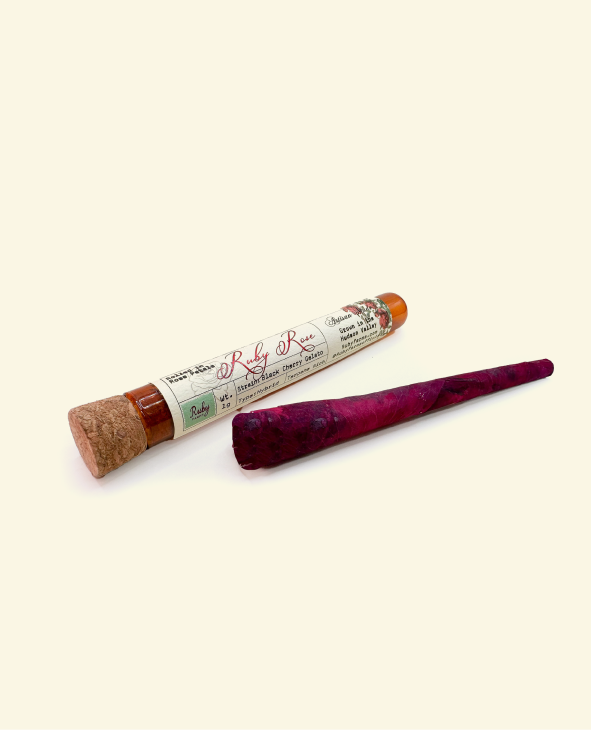 Glass tube labeled Ruby Rose next to a tightly rolled dark purple cone on a light background.
