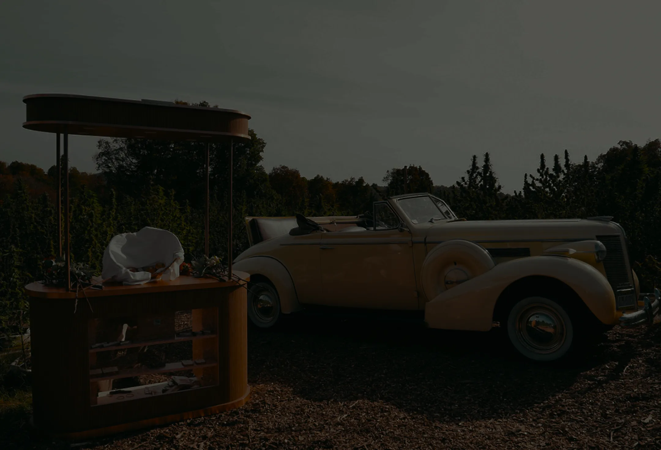 Vintage cream convertible car parked beside an empty wooden vendor kiosk outdoors.