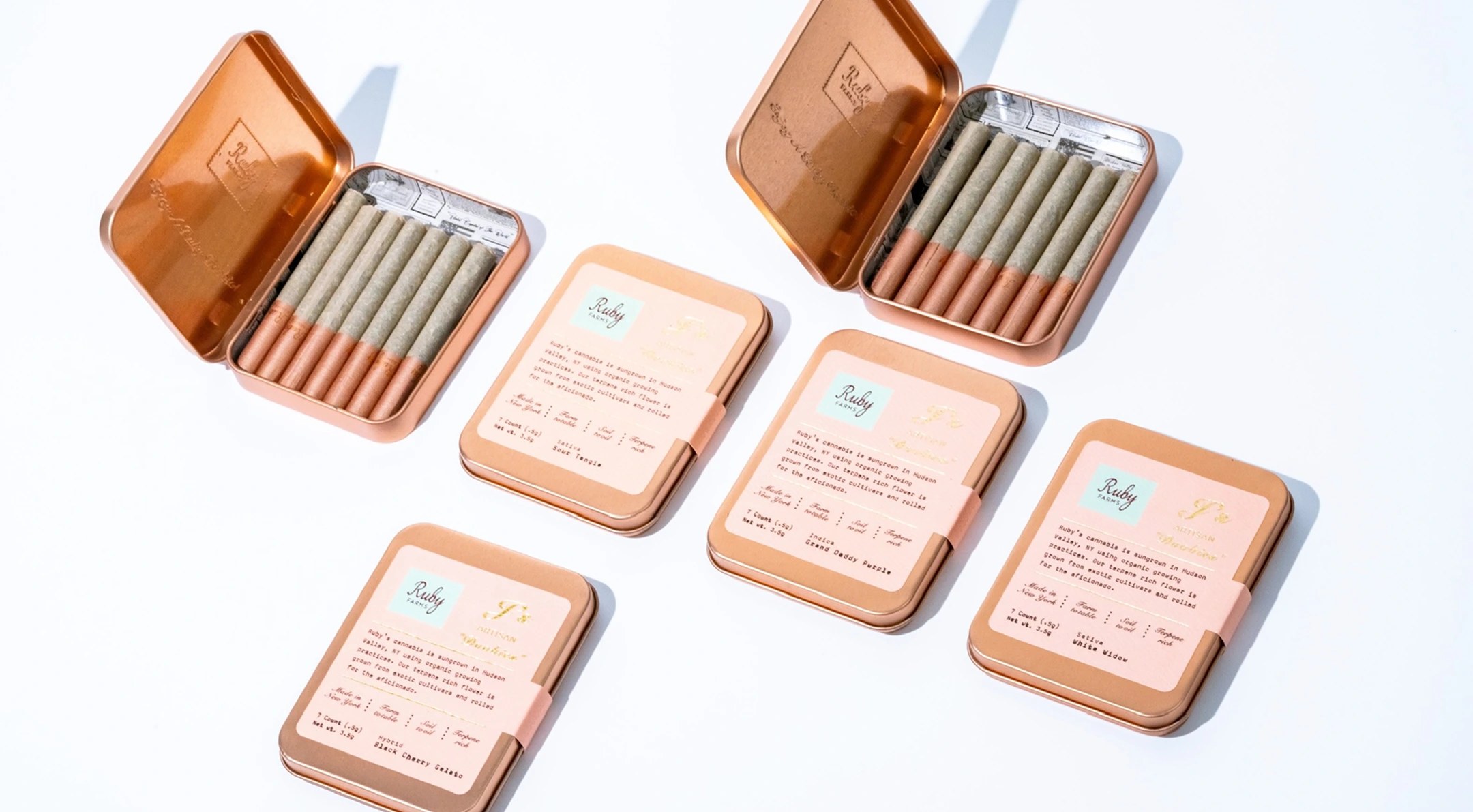 Four closed and two open metal tins of pre-rolled cannabis joints arranged on white surface.