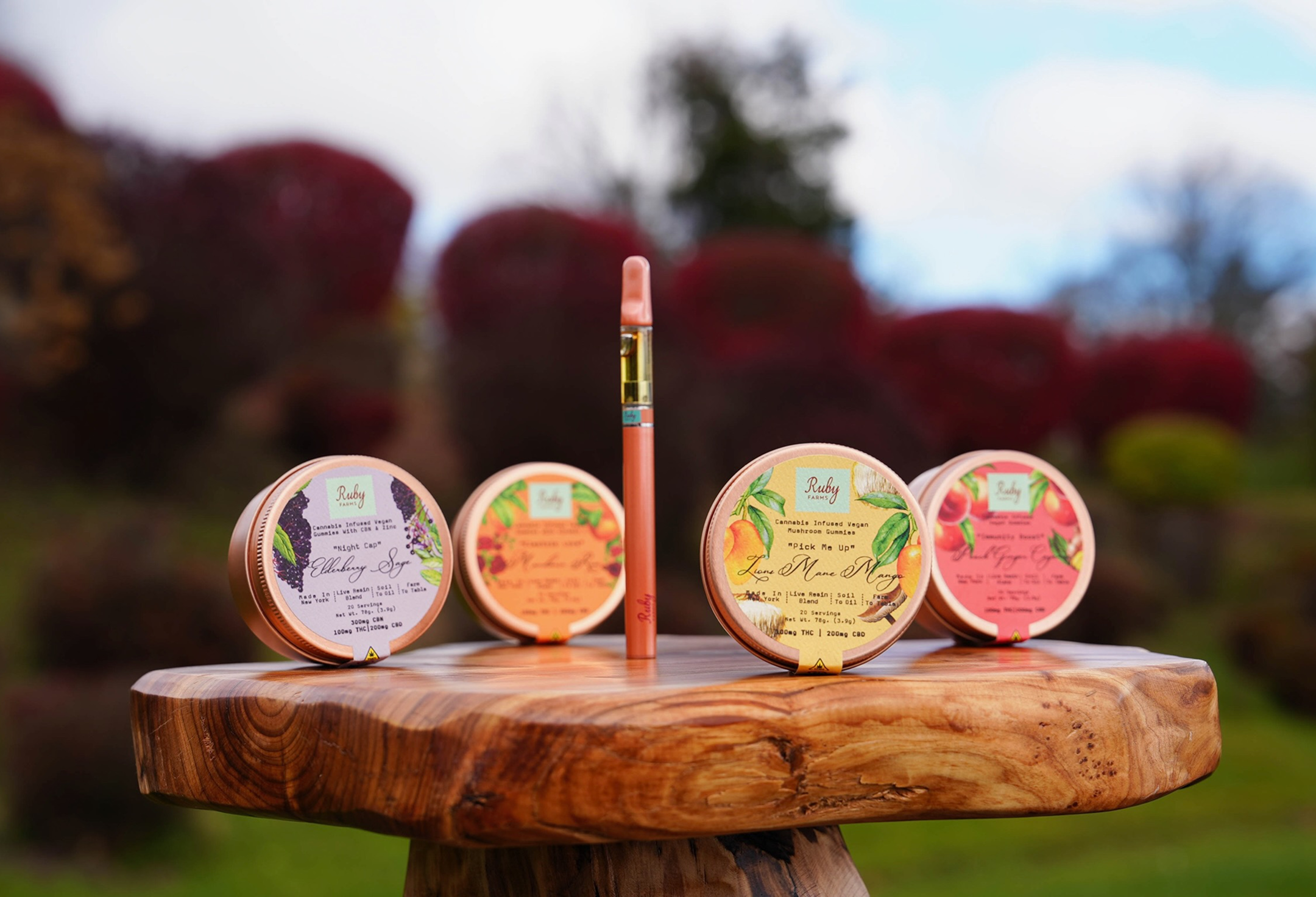 Cannabis-infused vegan gummies and vape pen displayed on a wooden stand outdoors.