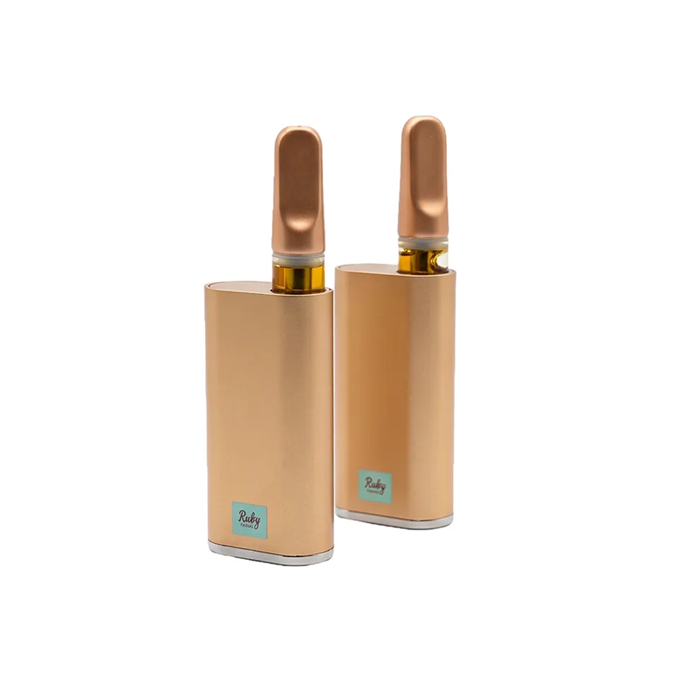 Bronze vape pens and cartridge with amber oil, labeled Ruby Farms, on wooden surface with forest background.