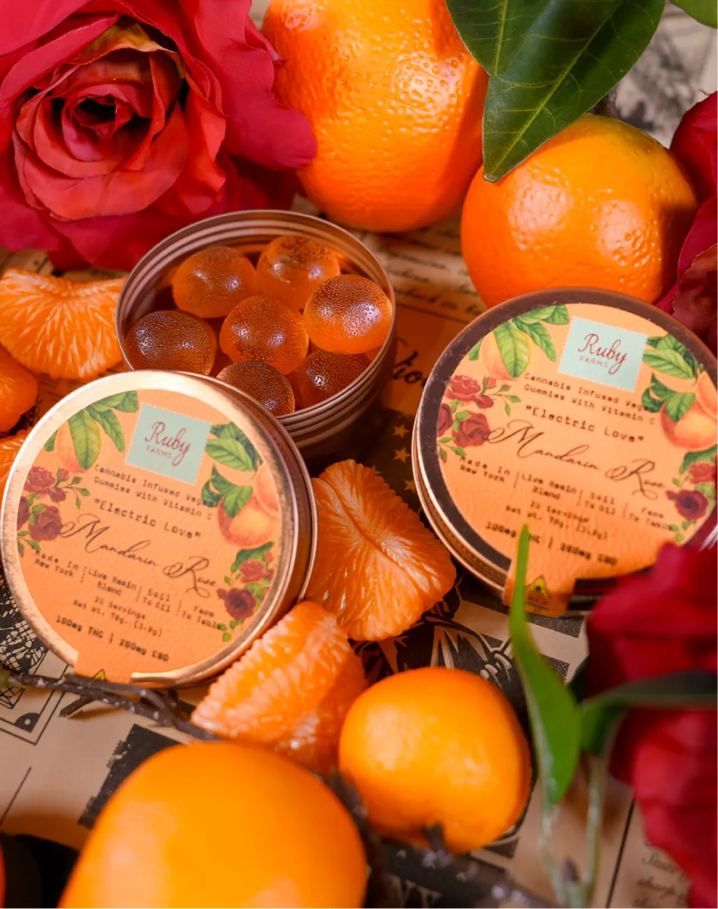 Open tins of cannabis-infused gummy candies surrounded by mandarin oranges and red roses.