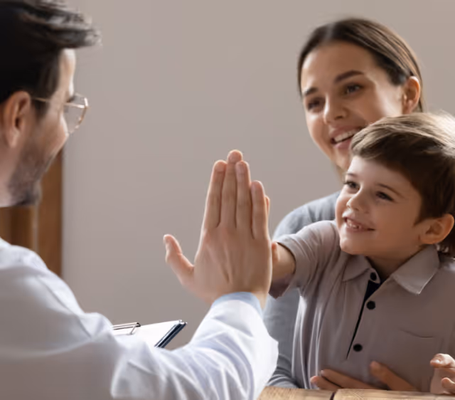 Young boy giving a high five to a doctor while sitting on his mother's lap.