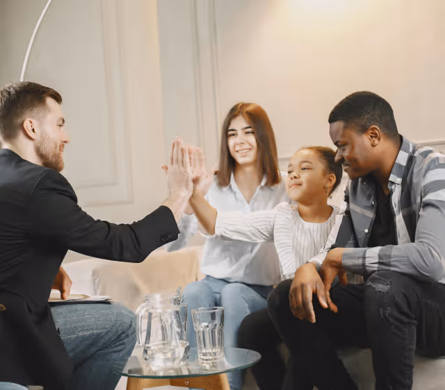 A diverse family happily giving high fives to a man in a suit in a cozy living room setting.