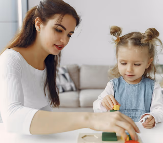 A woman and a young girl playing with colorful blocks together at a table in a cozy living room.