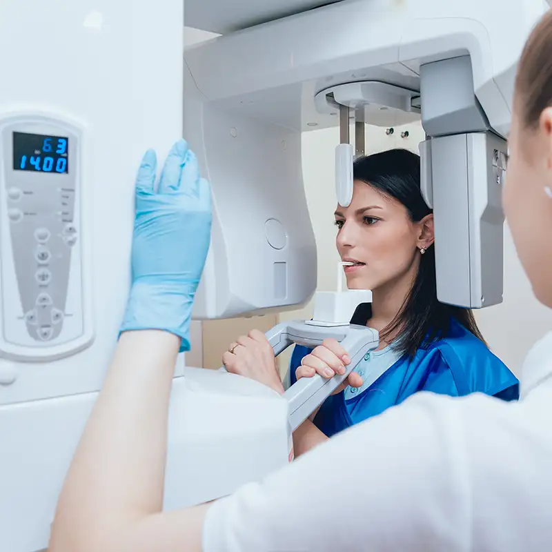 Woman undergoing a dental X-ray scan with a technician adjusting the machine.