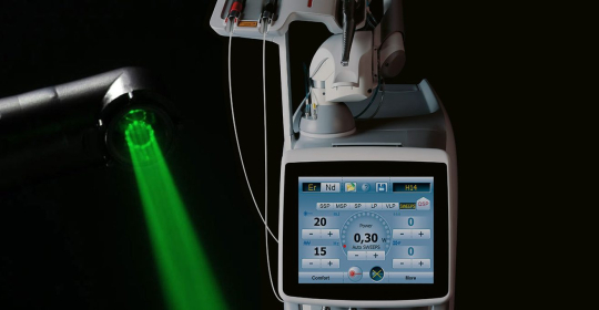 Medical laser device emitting a green laser beam with an illuminated control screen showing settings and power levels.