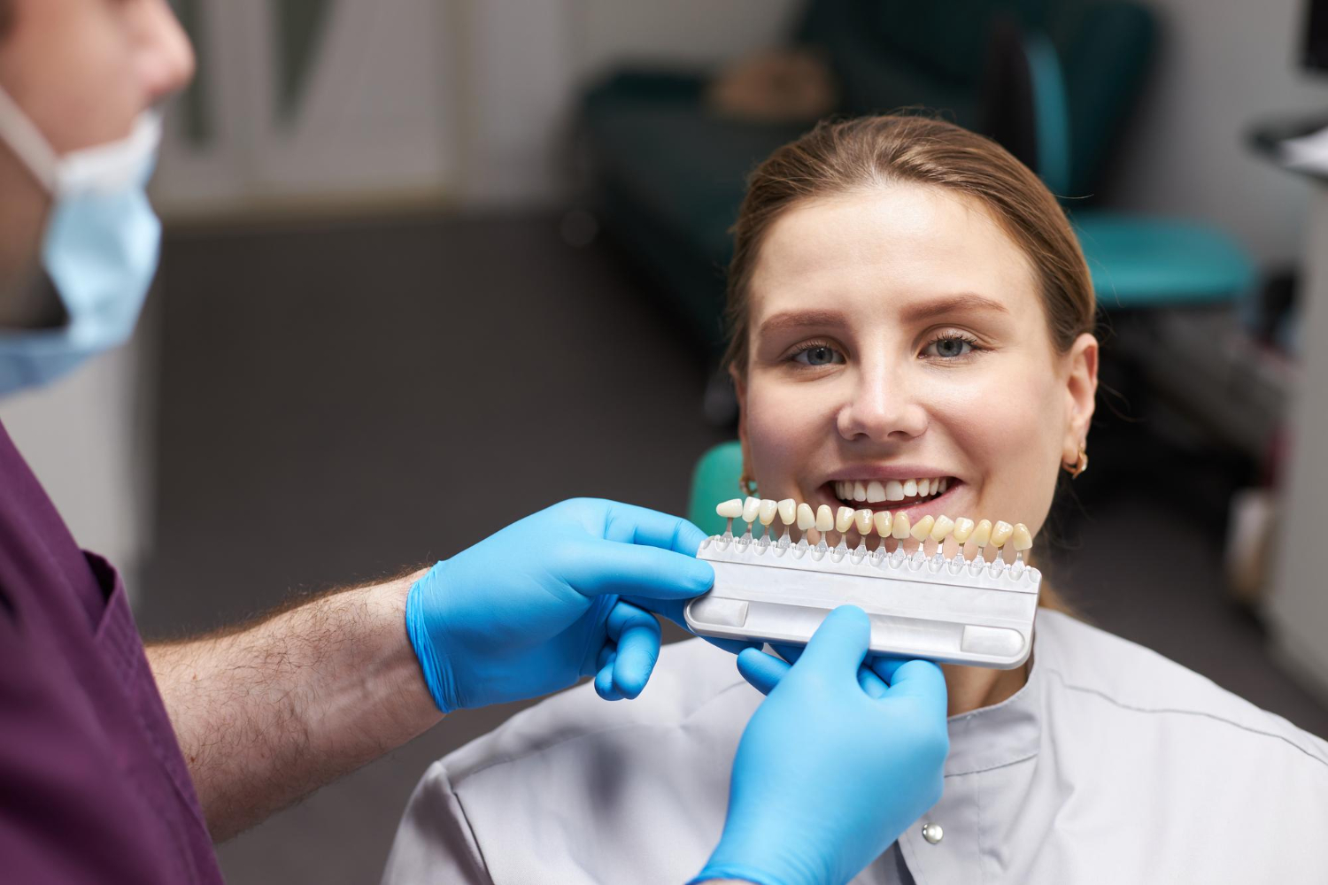 Dentist holding a shade guide next to a smiling patient's teeth to match dental crown color.