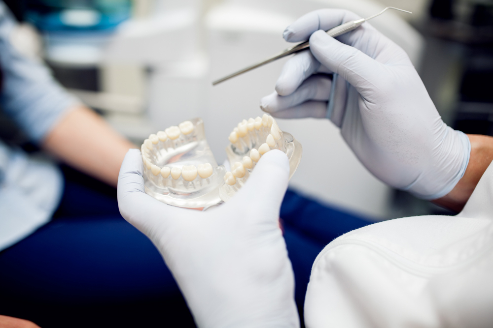Dentist wearing gloves holding dental mold and a dental tool during a consultation.