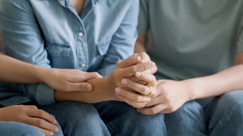 A family sitting together on a couch, holding each other's hands in a moment of connection and support during a counseling session.