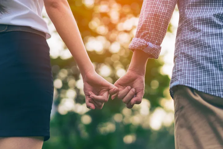 A couple gently holding hands while walking outdoors in warm sunlight, representing the connection and hope that marriage counseling can restore.